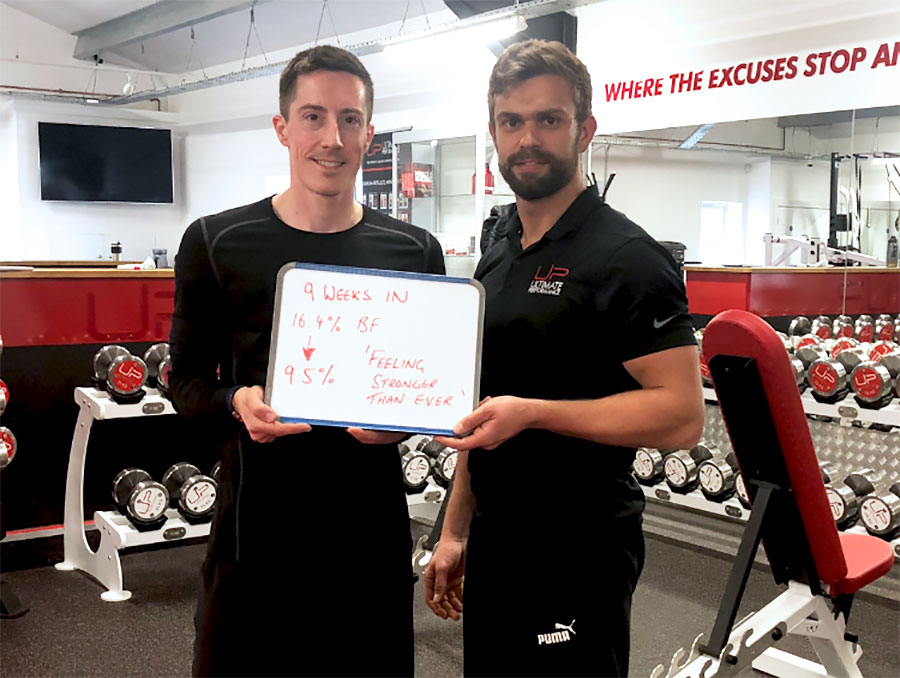  David-in-gym-with-trainer-and-sign Ultimate Performance